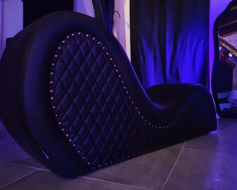 Le salon des envies Sofa tantra noir en forme ondulée avec des clous décoratifs, mirroir rétro-éclairé par une lumière violette.